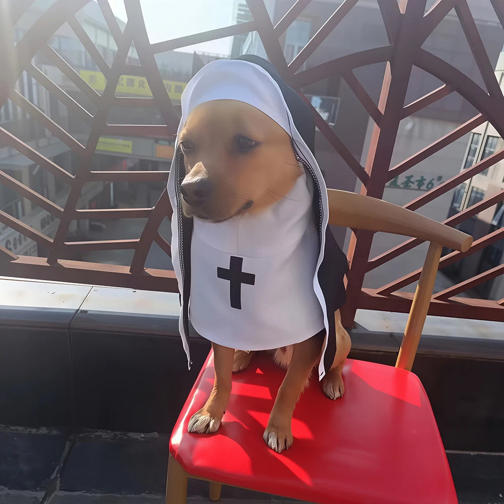 A small dog wearing a nun costume sits on a red chair in front of a balcony railing. The costume includes a white habit with a black cross on the chest and a black outer layer.
