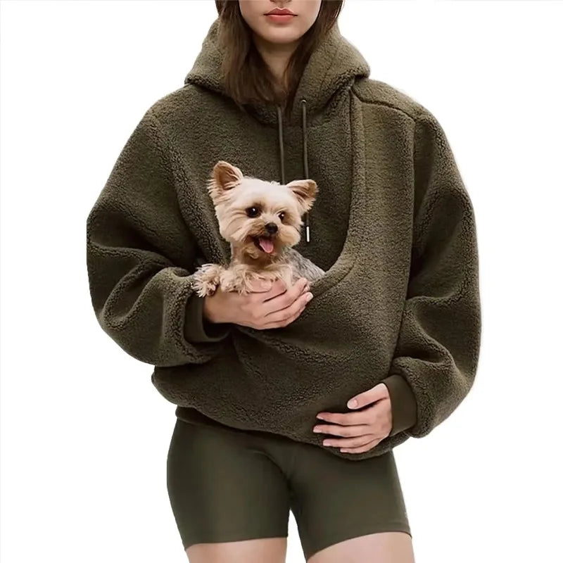Person wearing a green fleece hoodie holding a small dog on a white background