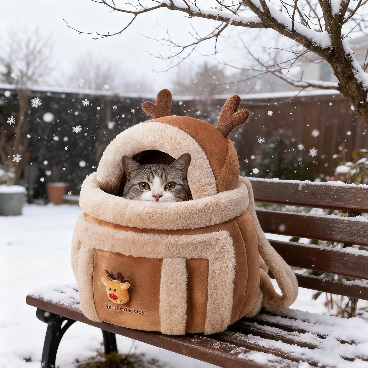 Cat in a reindeer-themed pet carrier on a snow-covered bench