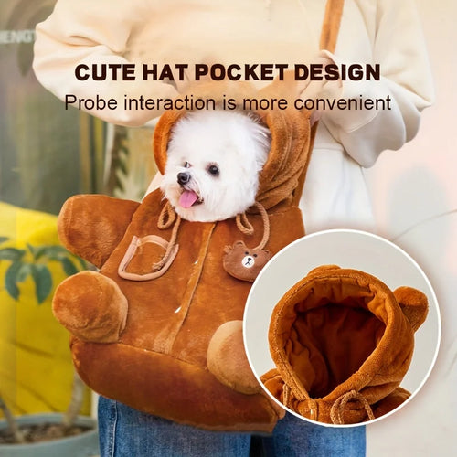 A small white dog sits inside a plush brown bear-shaped pet carrier bag worn crossbody by a person. The bag has a hood, drawstrings, and a small embroidered bear face patch.