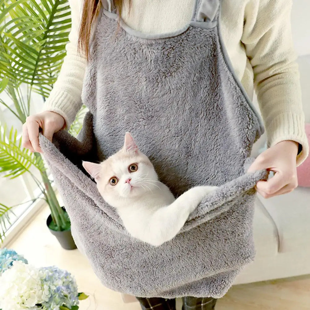 Person holding a fluffy gray pet sling with a white cat inside, indoor setting with plants and flowers.