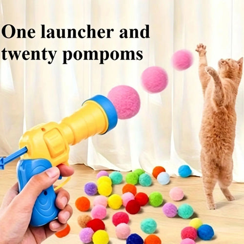 A hand holds a yellow and blue toy pom-pom launcher, launching pink pom-poms toward a standing orange cat in front of white curtains. Text at the top reads 'One launcher and twenty pompoms.