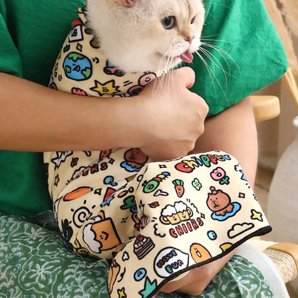 Person holding a cat wrapped in a colorful towel with cartoon designs.