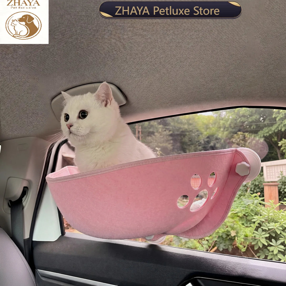 A white cat sits in a pink pet bed mounted on a car window, with a visible outdoor scene through the window and a 'ZHAYA Petluxe Store' logo banner at the top.