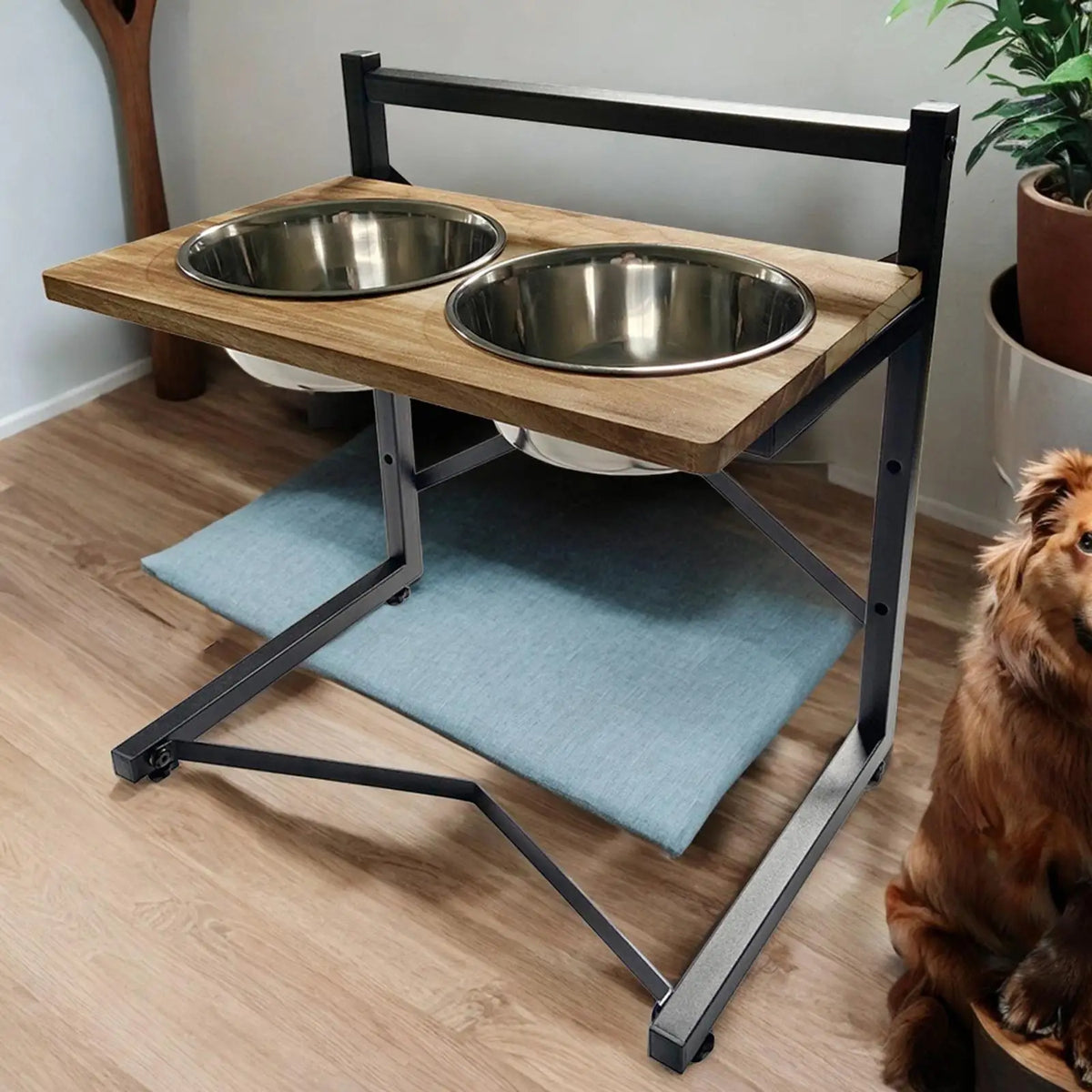 A two-bowl elevated pet feeder and water fountain stand with a light wood top, stainless steel bowls, and a black metal frame, shown in a home setting with a dog partially visible on the right.