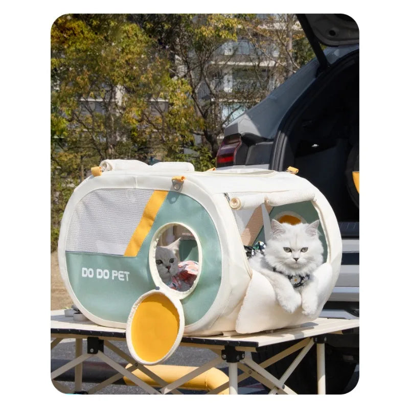A white fluffy cat sits inside a portable round cat carrier tent with mint green panels and yellow accents, placed on a folding table next to an open car trunk outdoors.