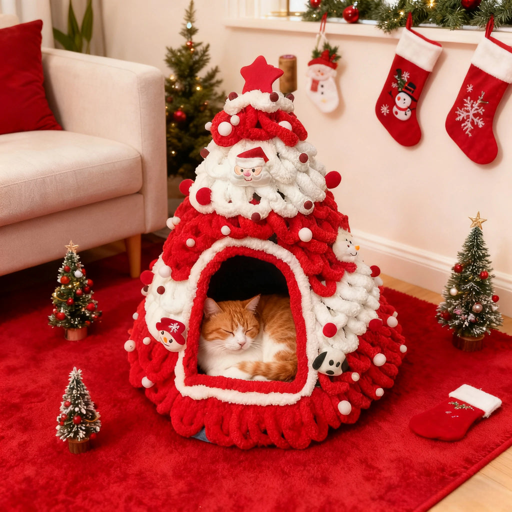 A fluffy red and white Christmas tree-shaped cat bed with a sleeping orange tabby cat inside, styled in a cozy holiday living room with miniature Christmas trees, stockings, and a red rug.