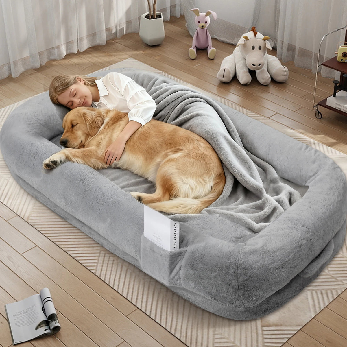 Woman and dog lying on a large gray pet bed in a room with toys in the background.