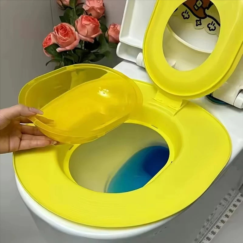 Yellow potty seat on a toilet with a hand holding one of its lids, against a neutral background.