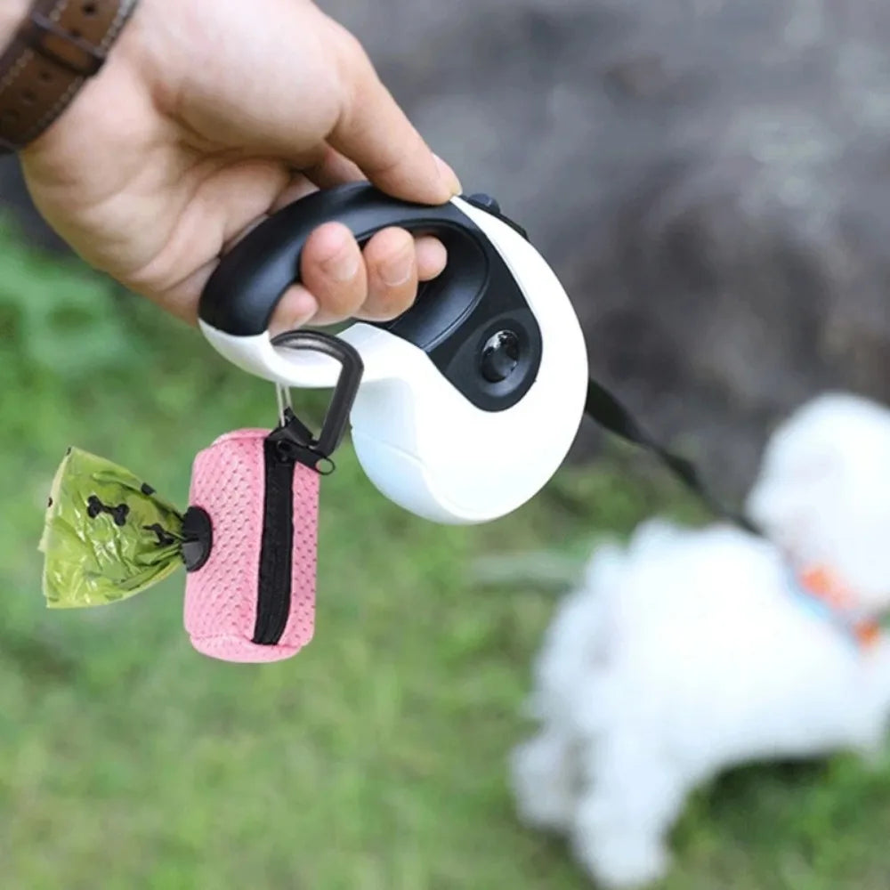 Person holding a white dog leash with a pink waste bag holder, dog in the background