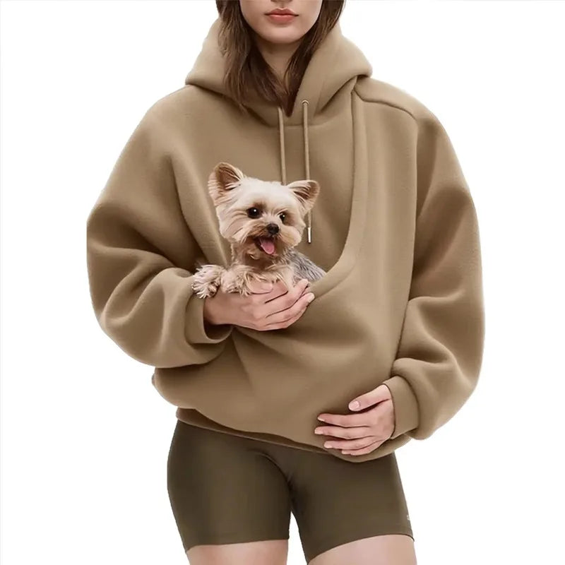 Person wearing a beige hoodie with a dog pocket, holding a small dog inside.