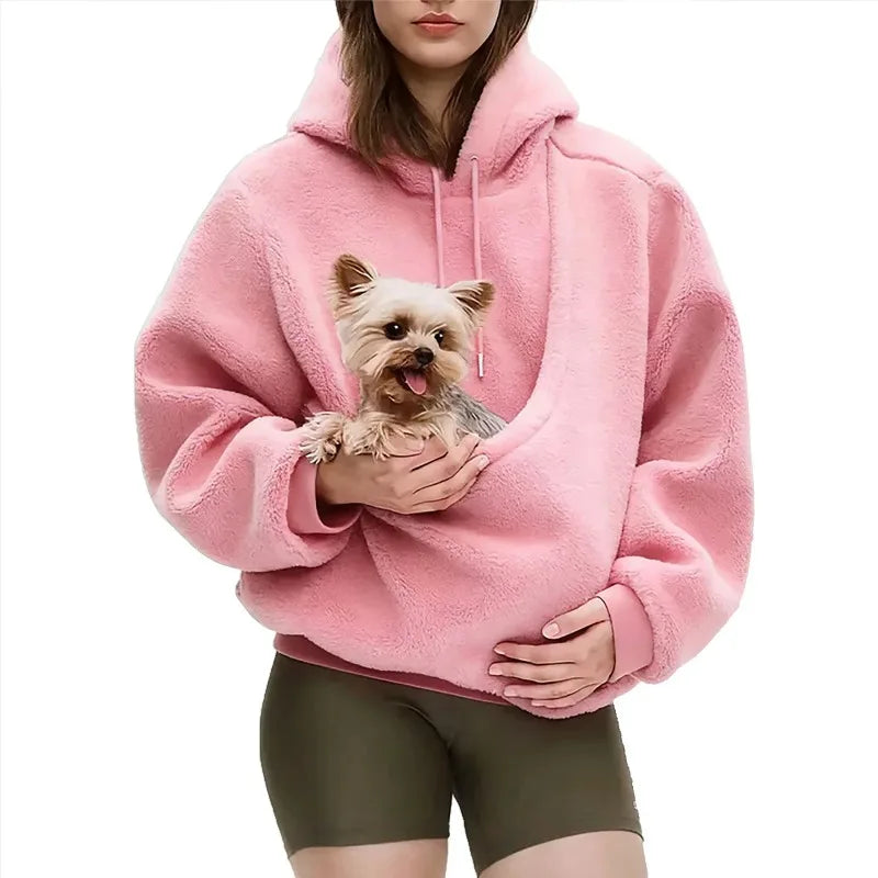 Person wearing a pink fleece hoodie with a small dog inside, on a white background