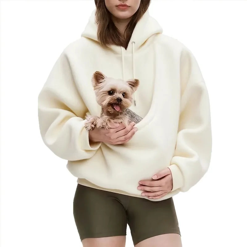 Person wearing a cream hoodie with a dog design, holding a small dog.