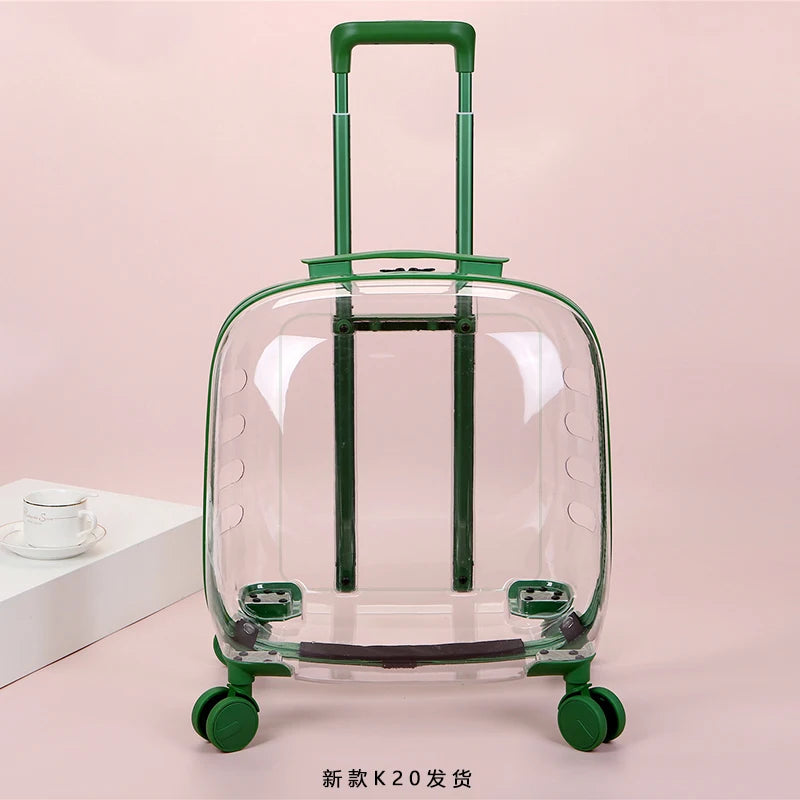 A clear hard-shell rolling suitcase with a green telescoping handle and green wheel bases, shown upright on a pale pink studio background. A small white cup sits on a pedestal to the left as a prop.