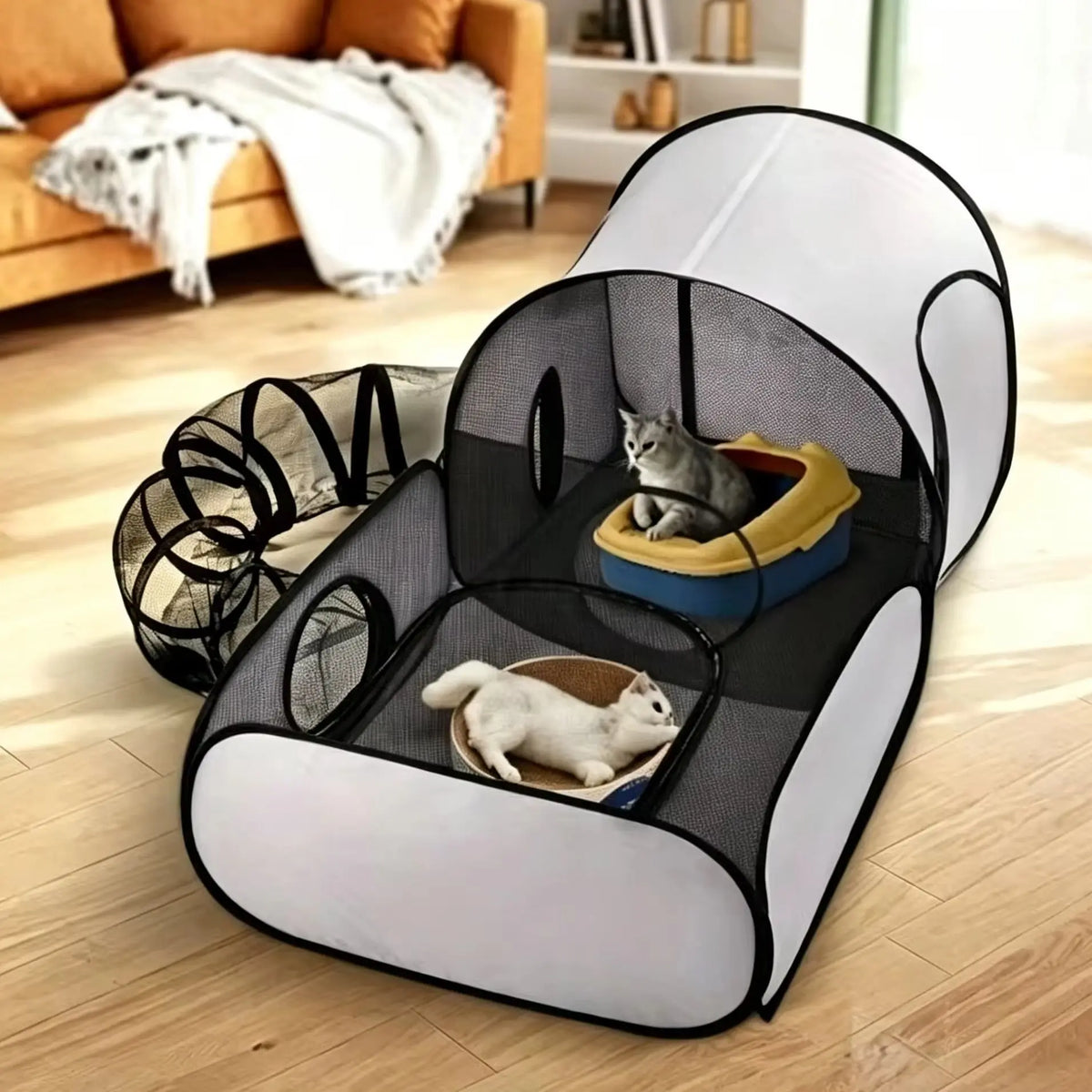 A pop-up cat play tent with mesh walls and a tunnel, shown in a living room with two cats inside. The tent has a white and black color scheme, and the scene is set on a light wood floor with a sofa in the background.